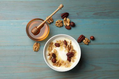 Delicious Greek yogurt with honey and nuts served on blue wooden table, flat lay