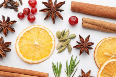 Farklı baharatlar, kızılcıklar, kuru portakal dilimleri ve beyaz masada taze biberiye, düz uzanmış.