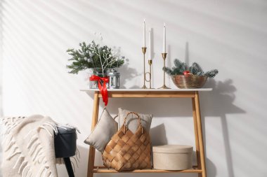 Konsol masasında farklı bir Noel dekoru ve kapalı alanda beyaz duvarın yanında puf.