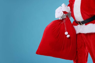 Noel Baba açık mavi arka planda torba tutuyor, mesaj için yere yakın çekim yapıyor. Mutlu Noeller ve mutlu yıllar.