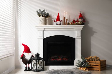 Christmas decor on fireplace and firewood near white wall indoors. Interior design
