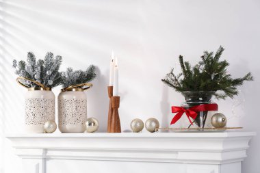 Beyaz duvarın yanındaki şöminede Noel süsü ve yanan mumlar.