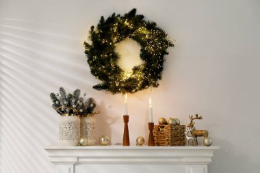 Beyaz duvarın yanındaki şöminede Noel süsü ve yanan mumlar.