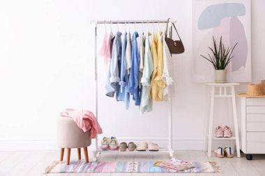 Beyaz duvarın yanında askıda asılı farklı şık kıyafetler, çanta ve ayakkabılar.