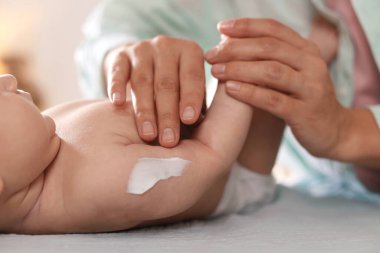 Anne bebeğinin koluna krem sürüyor evde masasını değiştiriyor, yakın plan.