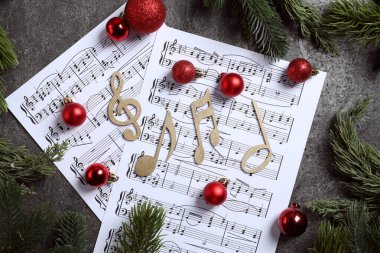 Gri desenli masa üzerinde altın müzik notaları, çarşaflar ve Noel süslemeleri.