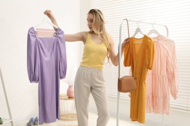 Kadın içeride menekşe ve turuncu elbiseler arasında seçim yapıyor.