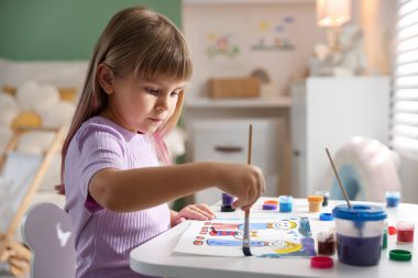 Beyaz masa içinde fırça çizen küçük kız.