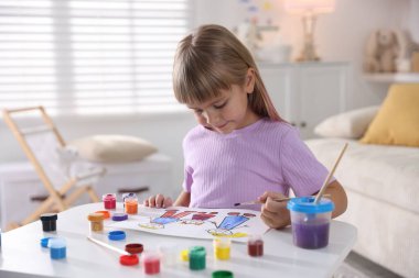 Beyaz masa içinde fırça çizen küçük kız.