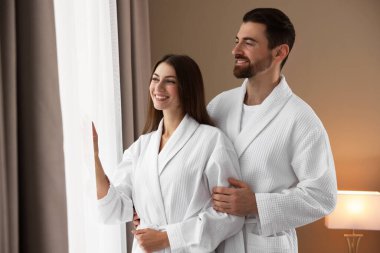 Otel odasının penceresinin yanında bornoz giyen mutlu çift.