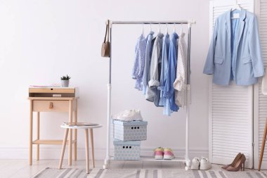 Beyaz duvarın yanında askıda asılı farklı şık kıyafetler, çanta ve ayakkabılar.