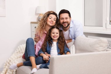 Mutlu ebeveynler ve kızları evdeki kanepede birbirlerine sarılıyorlar. Aile bağı