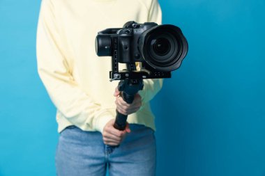 Açık mavi arkaplanda kamerası olan titreşimli dengeleyici kullanan kameraman, kapat