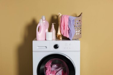 Modern çamaşır makinesi, deterjan ve zeytin duvarının yanındaki kıyafetler.