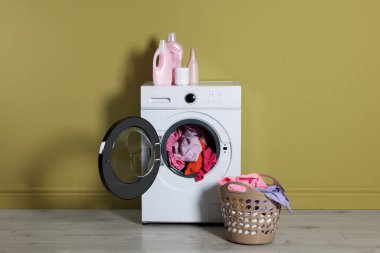 Modern çamaşır makinesi, deterjan ve zeytin duvarının yanındaki kıyafetler.