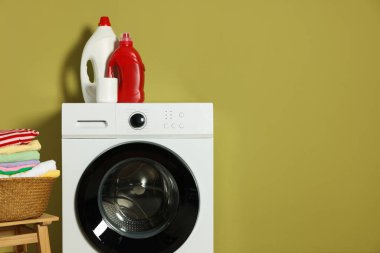 Modern çamaşır makinesi, deterjanlar ve zeytin duvarının yanındaki giysiler.