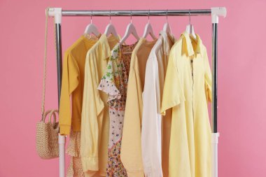 Farklı şık kıyafetler ve çanta pembe arka planda asılı duruyor, yakın plan.