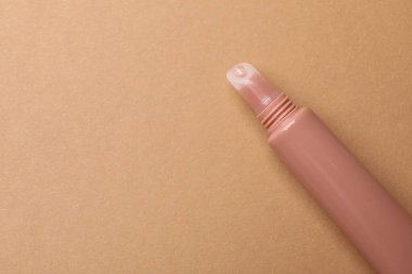 Beautiful nude lip gloss on brown background, top view. Space for text