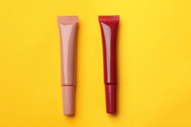 Sarı arkaplanda farklı dudak parlatıcıları, düz yatış