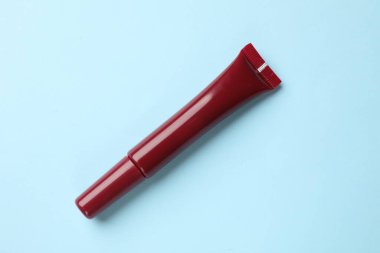 Açık mavi arkaplanda koyu kırmızı dudak parlatıcısı.