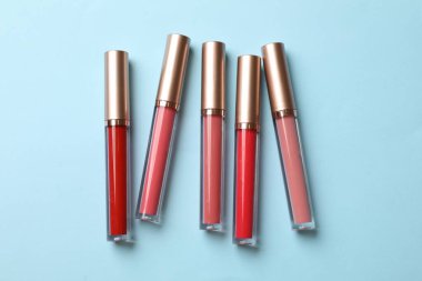 Açık mavi arkaplanda farklı dudak parlatıcıları, düz yatış