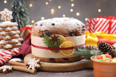 Baharatlı panettone keki, şekerli meyveler ve kahverengi masanın üzerindeki Noel süsü bulanık ışıklara karşı, yakın plan. Bokeh etkisi