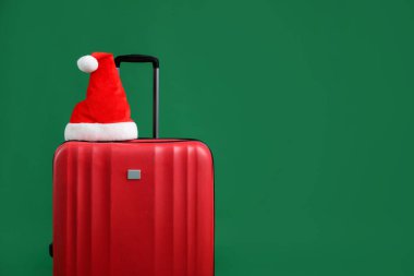 Kırmızı bavulda Noel Baba şapkası yeşil arka planda, mesaj için yer var. Noel tatili