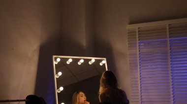 Güzel elbiseli çekici bir kadın aynanın yanına ruj sürüyor, kamera aşağı iniyor.