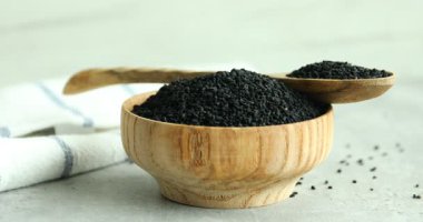 Gri masadaki ahşap kaseye aromatik siyah oyma döken kadın, yakın plan.