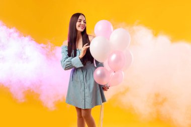 Turuncu arka planda balonları olan güzel bir kadın.