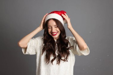 Noel Baba şapkalı güzel kadın gri arka planda eğleniyor. Noel partisi