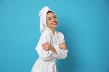 Açık mavi arka planda, havluya sarılı saçı olan bornoz giyen bir kadın. Metin için boşluk