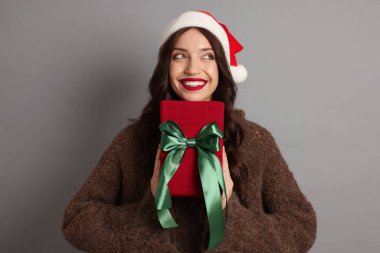 Mutlu kadın gri arka planda Noel hediyesi olan Noel Baba şapkası takıyor.