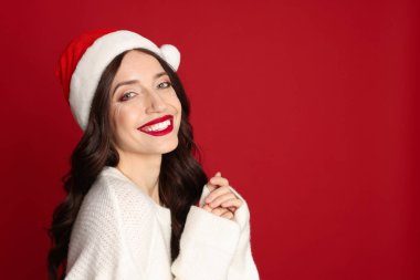 Kırmızı arka planda Noel Baba şapkalı güzel bir kadın, mesaj için yer var. Noel sezonu