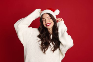 Kırmızı arka planda Noel Baba şapkalı güzel bir kadın. Noel sezonu