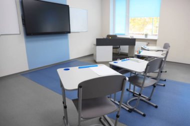 Okulda masaları, sandalyeleri ve televizyonu olan şık bir sınıf.