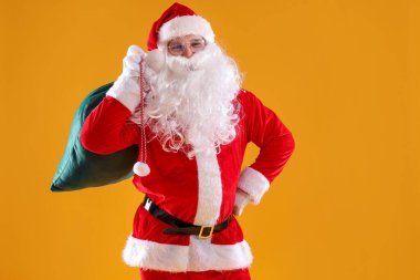 Sarı arka planda çantası olan Noel Baba, mesaj için yer var. Mutlu Noeller ve mutlu yıllar.