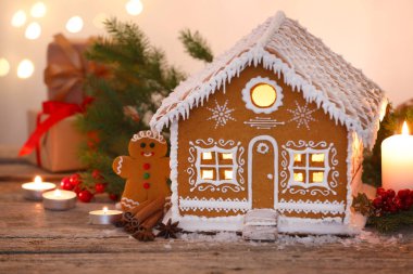 Güzel zencefilli kurabiye evi ve ahşap masanın üzerindeki Noel dekoru bulanık ışıklara karşı, yakın plan.