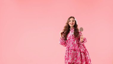 Pembe arka planda lolipopu olan güzel giyimli bir kadın.