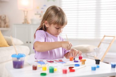 Beyaz masa içinde fırça çizen küçük kız.