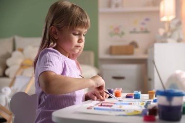 Beyaz masa içinde fırça çizen küçük kız.