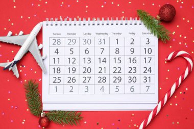 Noel tatili. Takvim, oyuncak uçak, dekor ve şeker bastonu kırmızı arka planda, düz yatıyordu