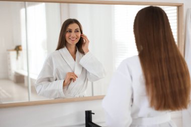 Güzel bir kadın beyaz bornoz giyiyor ve aynada kendine bakıyor.