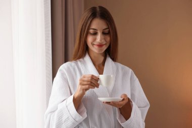 Bornozlu güzel bir kadın, pencerenin yanında sabah kahvesi var.