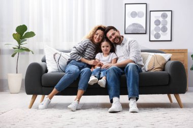 Mutlu ebeveynler evdeki kanepede kızlarına sarılıyorlar. Aile bağı