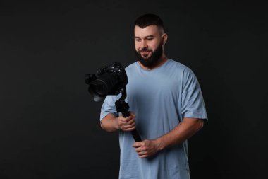 Kameraman siyah arkaplanlı, titreşimli dengeleyici kullanıyor. Metin için boşluk