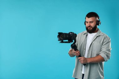 Kameraman açık mavi arkaplanda kameralı titreşimli dengeleyici kullanıyor. Metin için boşluk