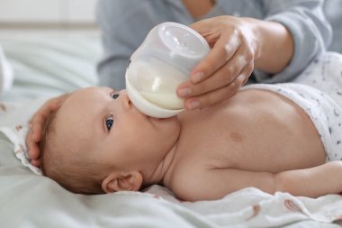 Anne bebeğini evde şişeyle besliyor, yakın plan.