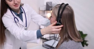 Duyma testi. Doktor klinikte hastanın işitsel kulaklığını ayarlıyor. Kamera sağa hareket ediyor