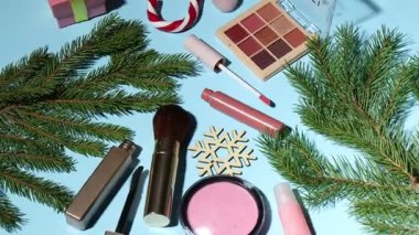 Açık mavi arka planda makyaj ürünleri ve Noel dekoru, üst görünümde
